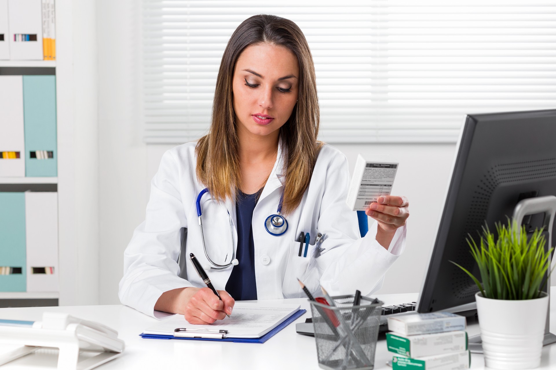 Female pharmacis writing notes with boxes of medicine in Hand