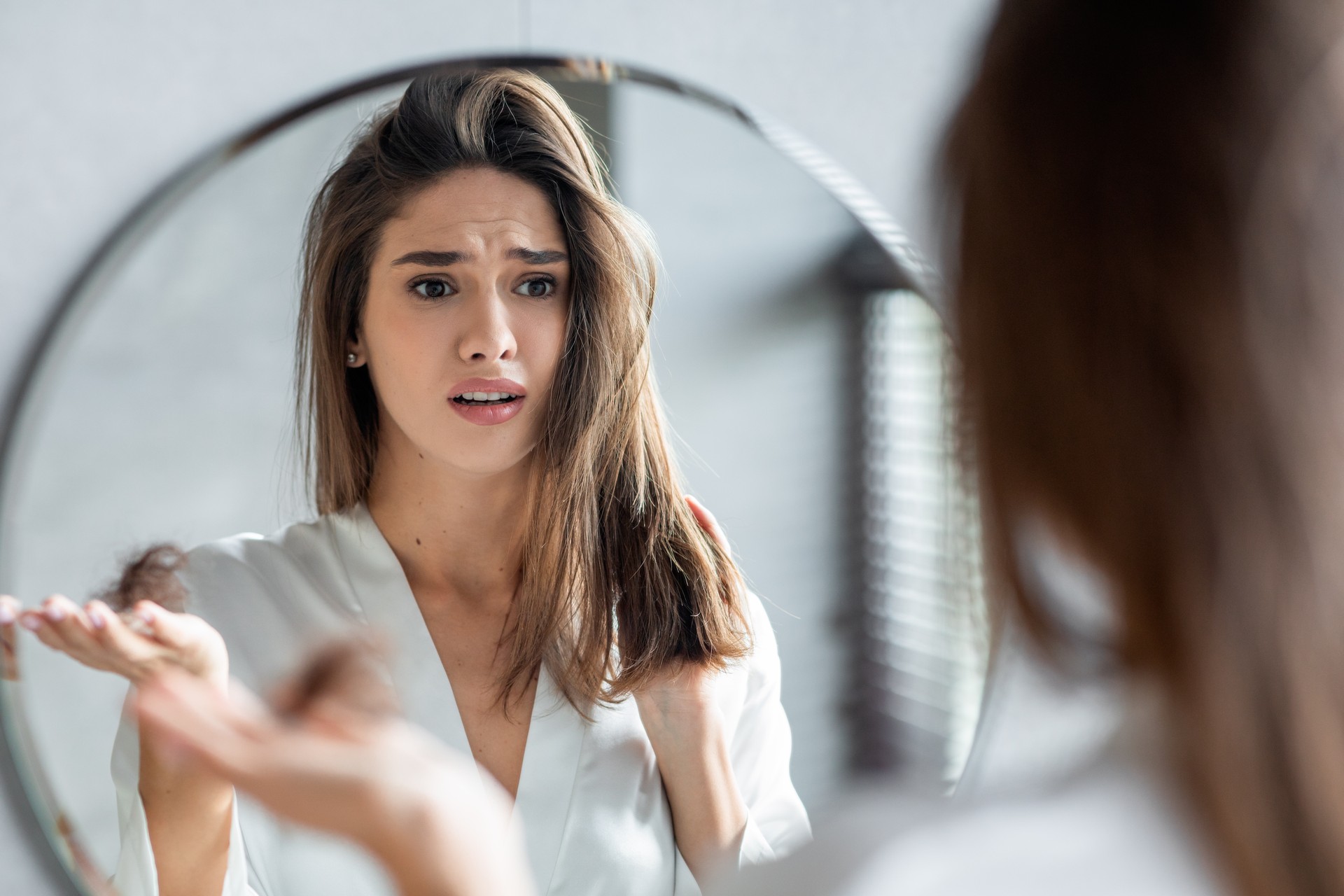 Woman concerned about hair loss, examining her hair in the mirror