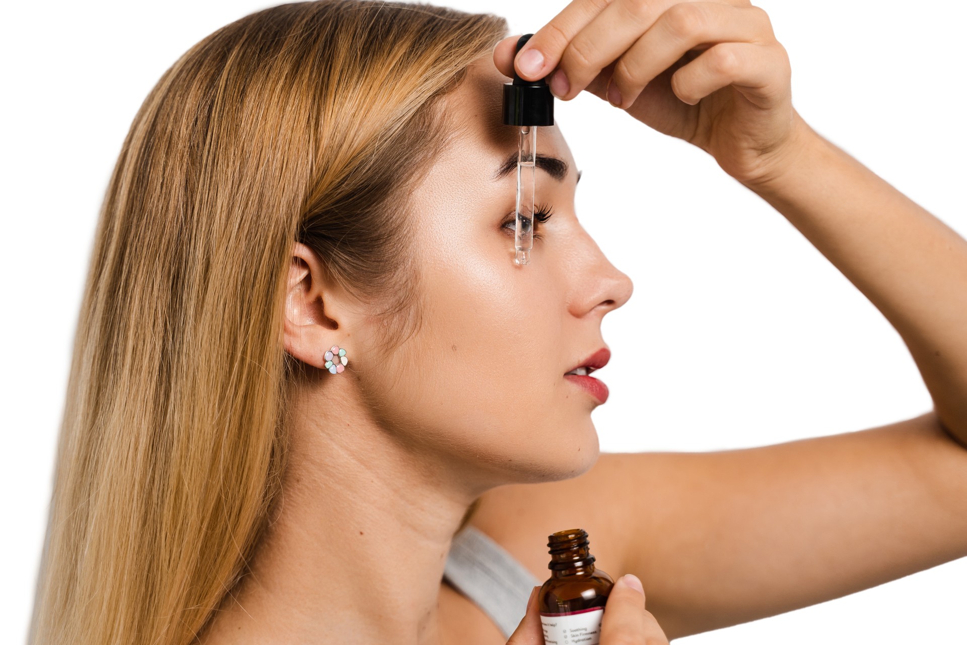 Woman applying a serum with a dropper to her hairline, focusing on treatment for thinning or growth stimulation.