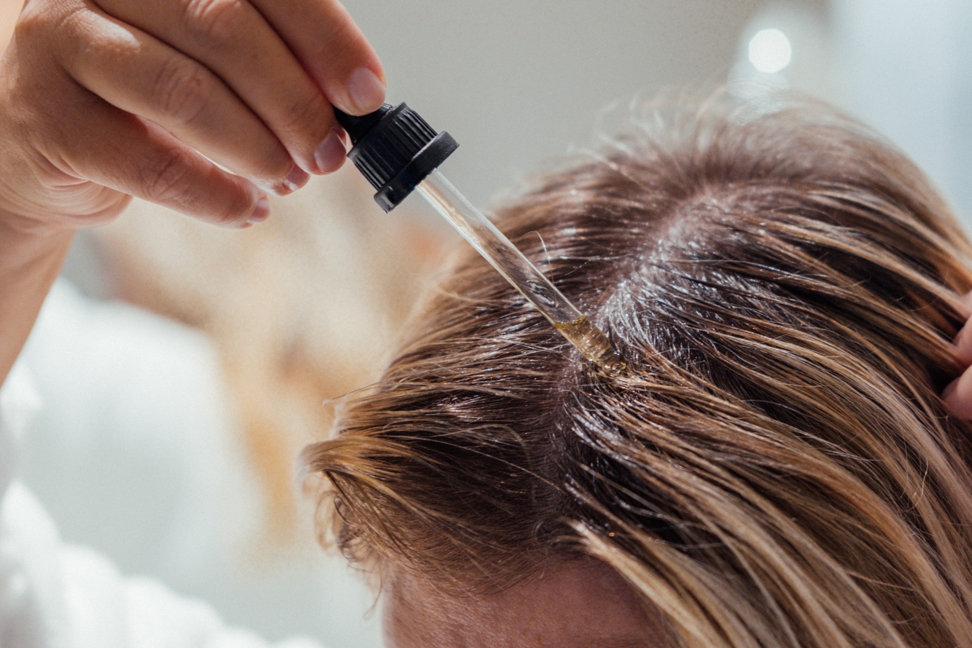 Close-up of a person applying a hair growth serum with a dropper to the scalp, targeting thinning areas for treatment.